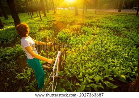 Girl on a bike in a forest glade with growing lilies of the valley at sunset