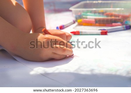 Close-up of a child's hand drawing with multicolored pastel crayons on a large sheet of white paper