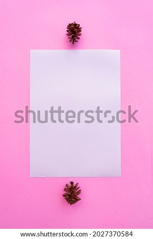 A4 White Paper On Pastel Pink Background With Spruce Flower Decoration. Vertical Photo, White Paper. Paper Mockups. Pastel Color Background
