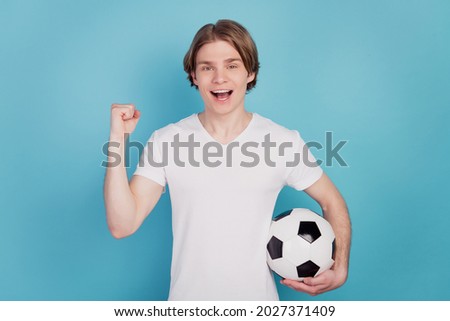 Photo of positive man holding soccer ball raise fists isolated blue background