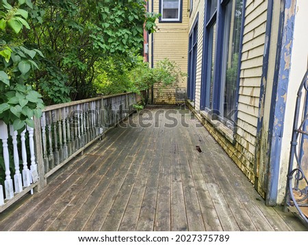 An old deck with holes in it outside of a building. The decaying wood is rotten and a safety hazard to those walking along the damaged deck attached to the abandoned building. Royalty-Free Stock Photo #2027375789