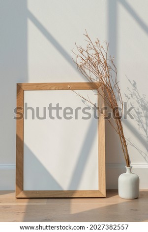 Dried white statice flower in a white vase by an empty wooden frame on a wooden floor