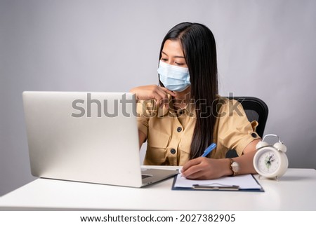 Female employee wearing medical facial mask working alone as of social distancing policy in the business office during new normal change after coronavirus or post covid-19 outbreak pandemic situation. Royalty-Free Stock Photo #2027382905
