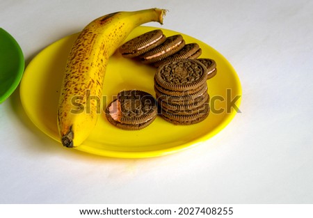  
Mysuru,Karnataka,India-August 19 2021; A Close up picture of creamy Biscuits and a ripe Banana for a fast bite on a yellow plate against a white background.
