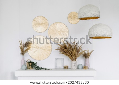 Design of room interior with natural decoration. Closeup at modern living room style, cozy rural apartment details. Wooden decor at wall, dry plants in vase, clay lamps hanging from above.