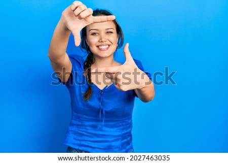 Young hispanic girl wearing casual clothes smiling making frame with hands and fingers with happy face. creativity and photography concept. 