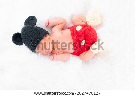 Cute little newborn boy wearing a black hat, cute red pants is sleeping in a white bed. Concept portrait studio fashion newborn.