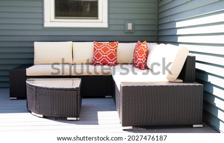 Outodoor wicker furniture on a composite deck against a green vinyle sided house.