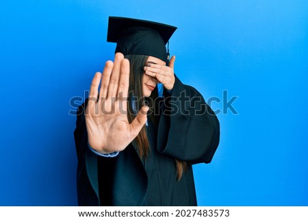 Beautiful brunette young woman wearing graduation cap and ceremony robe covering eyes with hands and doing stop gesture with sad and fear expression. embarrassed and negative concept. 