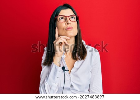 Young hispanic woman using lavalier microphone serious face thinking about question with hand on chin, thoughtful about confusing idea 