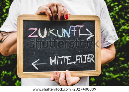 man with painted fingernails holds a sign with german text, concept lgbt and diversity. text means future and medieval