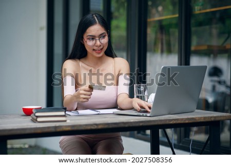 Portrait of Cute woman holding white credit card for shopping online with computer while sitting in living room at home.