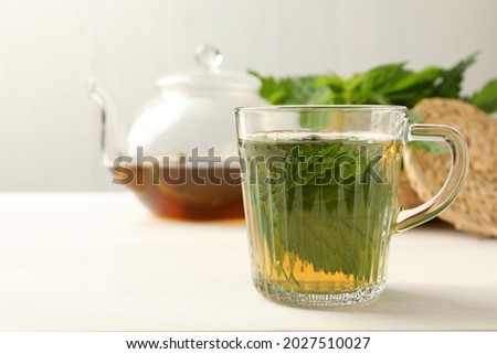 Glass cup of aromatic nettle tea on white wooden table, space for text
