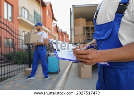 Moving service workers outdoors, unloading boxes and checking list Royalty-Free Stock Photo #2027517479
