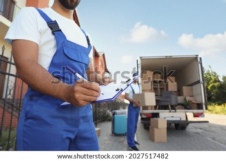 Moving service workers outdoors, unloading boxes and checking list Royalty-Free Stock Photo #2027517482