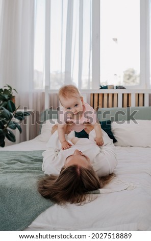 mom is lying on the bed and lifts up the baby girl