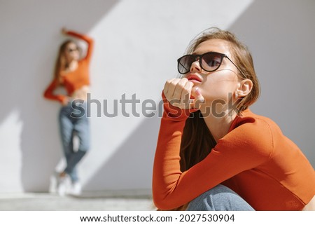 Portrait of twin sisters in sunglasses and identical clothes posing in contrast sunlight outdoors. Focus on foreground. 