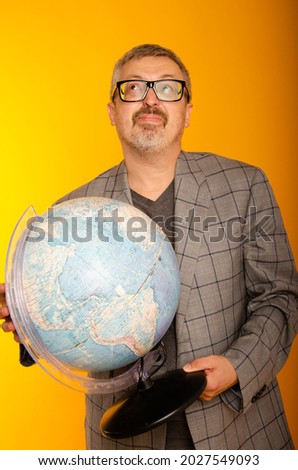 A man of American appearance with a globe in his hands on a yellow background Geography teacher at school. Grandpa is in a great mood with joyful emotions. Place for text.