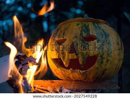 carved eyes and grin on a pumpkin for a Halloween party. Close-up view of a scary pumpkin next to a fire flame, on a dark dusk background. light and dark