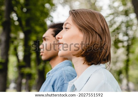 Young mixed-race boyfriend and girlfriend woman and man looking far away together in the same direction. Young students friends walking outdoors in park together. Royalty-Free Stock Photo #2027551592