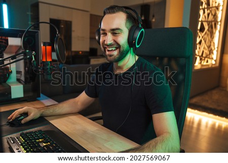 Happy young man gamer streamer in headphones playing on computer talking with players on chat in gaming competition Royalty-Free Stock Photo #2027569067