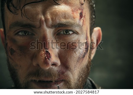 Cropped close-up portrait of one brutal bearded man, medeival warrior or knight with dirty wounded face isolated over dark background.