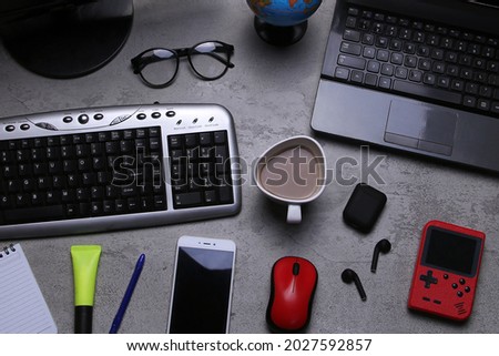 Top view. Work equipment on the table texture. Computer, laptop, keyboard, mouse, smartphone, earphone, notebook, globe, pen, highlighter, glasses, and a cup of coffee.