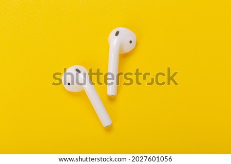 White wireless headphones with charging case on yellow background