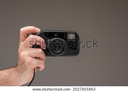 Caucasian male hand holding a generic old film point and shoot camera. Close up studio shot, isolated on brown background.