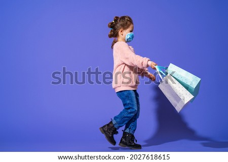 Stylish little girl in fluffy sweatshirts and jeans on a purple background. paper bags with purchases in the hands of a child. Emotional image.