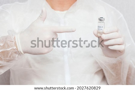 A male doctor holds a COVID-19 vaccine and points his finger in her direction. Healthcare And Medical Concept.