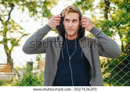 Young minded serious sportsman man 20s wearing grey sportswear hood headphones listen to music while training resting in leisure time at basketball playground court Outdoor courtyard sports concept.