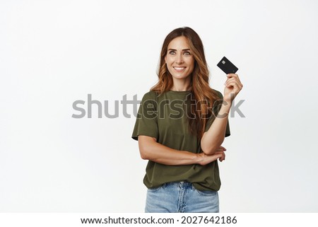 Smiling thoughtful woman looking aside, ready to use her credit card to buy smth, online shopping, using discount in store, standing against white background