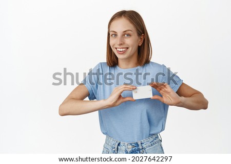 Image of happy young woman showing discount, credit card near heart, likes bank new offer, cashback or deposit proposal, smiling satisfied, white background