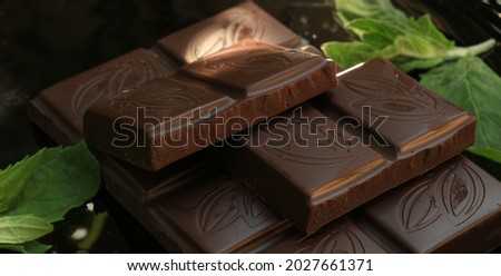 Luxury homemade dark sweet chocolate with organic mint in sun lights with a dark black background. New abstract wallpaper in luxury design with a picture of chocolate slices and mint leaves 