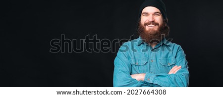 Handsome confident man is looking at the camera smiling with his arms crossed over black background.