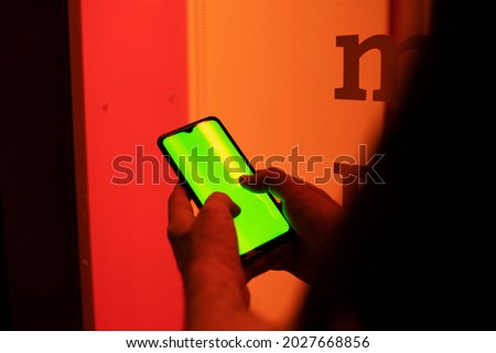 
man's hands writing on the screen of a cell phone in front of a red window at night