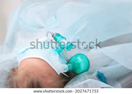 Child's face is covered with a mask. A breathing tube in the mouth. The child is under anesthesia. Preparing for surgery. Copy space.