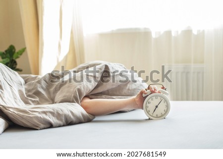 boy lying on the bed under a blanket and stopping alarm clock in the morning. childs hand reaching for the alarm clock to turn it off. Royalty-Free Stock Photo #2027681549