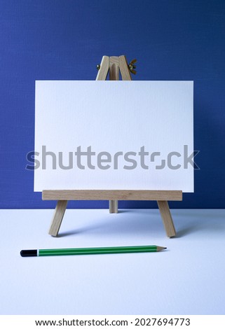 wooden easel with white board with space for text, blue background, green pencil.