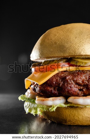 photo of a juicy burger with cutlet, salad, cheese, and fried shrimp which is painted with edible gold paint