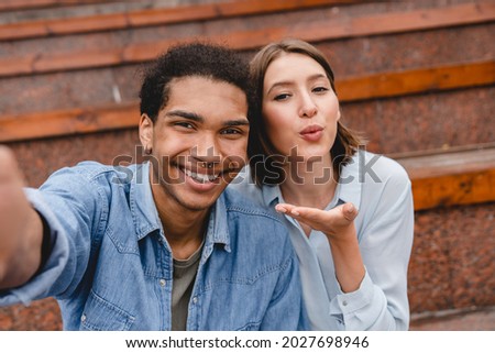 Young boyfriend and girlfriend mixed-race friends students taking selfie having video call conversation vlogging blogging online on smart phone while walking together on a date outdoors.