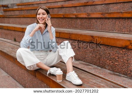 Young beautiful student woman girl talking on smart phone with perfect connection sitting on a bench. Young freelancer relaxing communicating with friends on cellphone outdoors.