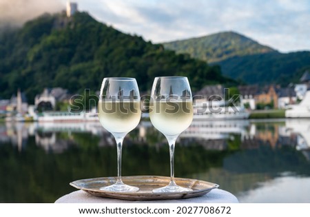 Tasting of white quality riesling wine served on outdoor terrace in Mosel wine region with Mosel river and old German town on background in sunny day, Germany Royalty-Free Stock Photo #2027708672
