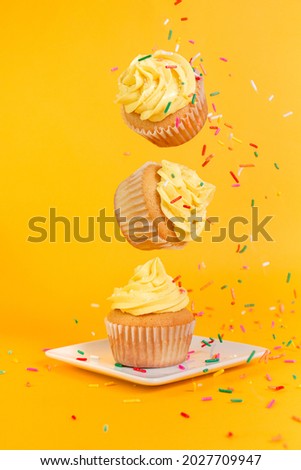 Vanilla cupcakes with yellow frosting and rainbow sprinkles floating on a yellow background