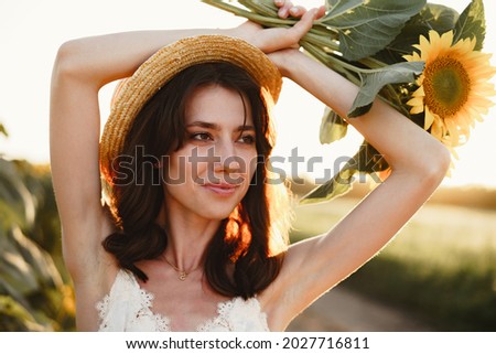 Young woman having a walk in sunflowers field in the morning