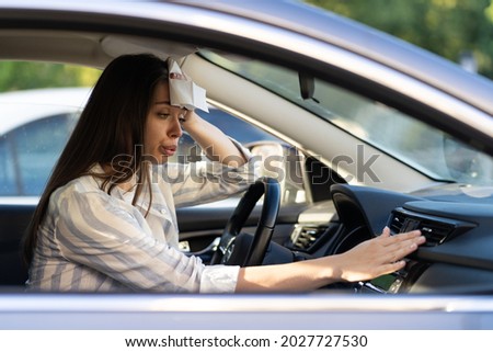 Exhausted young woman suffering from heat inside car with broken air conditioner. Female driver feeling sick and headache from hot air temperature in vehicle regulating condition panel knobs in summer Royalty-Free Stock Photo #2027727530
