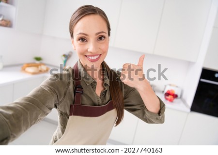 Photo of shiny adorable housemaid wear brown apron smiling showing thumb up recording video indoors room home house