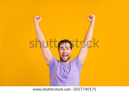 Photo of pretty lucky young guy dressed purple t-shirt yelling rising fists smiling isolated yellow color background