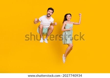 Photo of crazy married couple raise fists jump achieve goal wear casual outfit isolated yellow color background